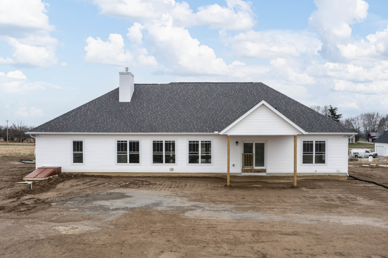 White house with black roof and chimney, dirt yard in foreground, large windows, cloudy sky above