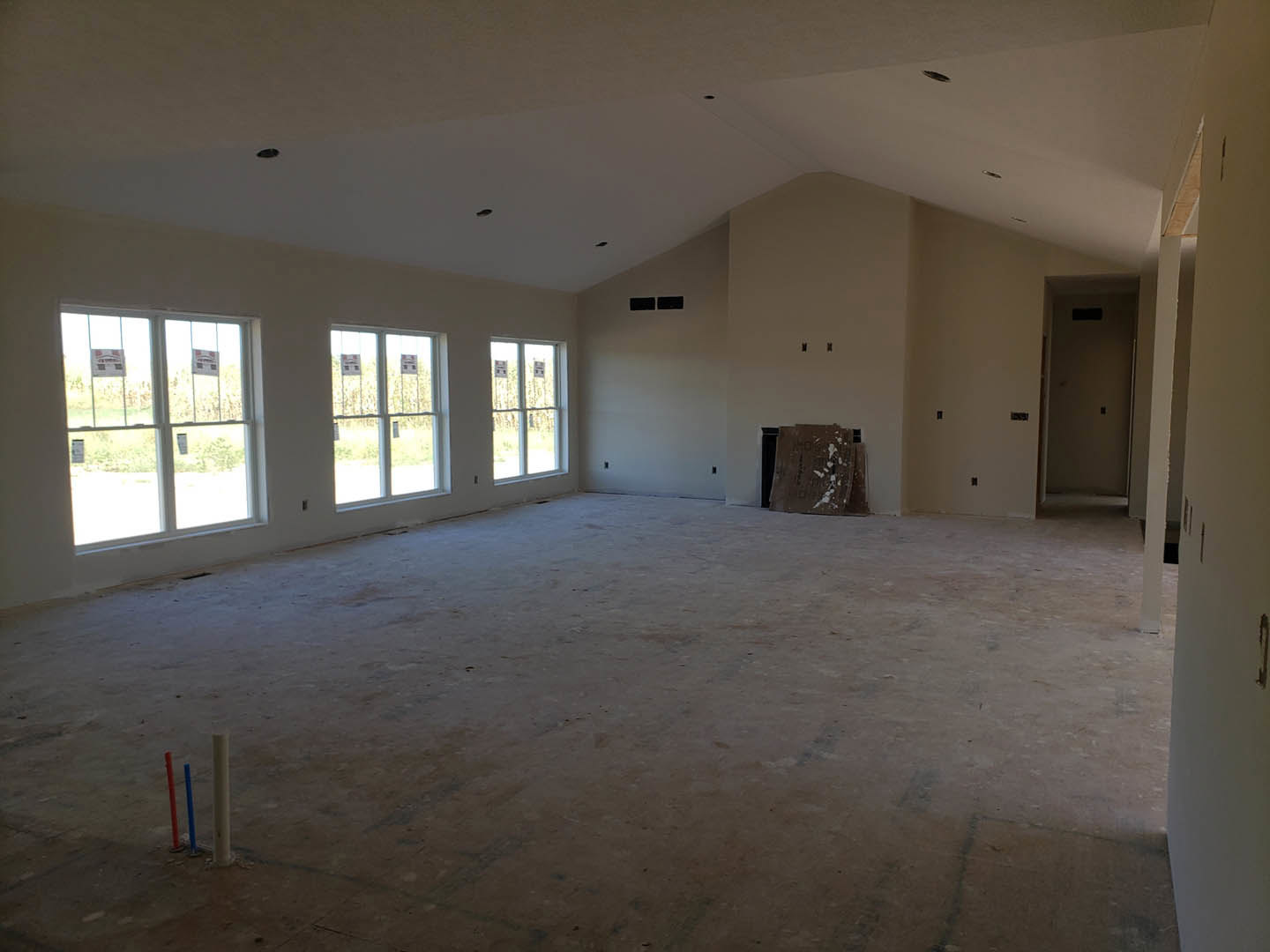 Bright room featuring multiple large windows, white plaster walls, light flooring, scattered cardboard pieces with white paint, and a white door with a black square accent.