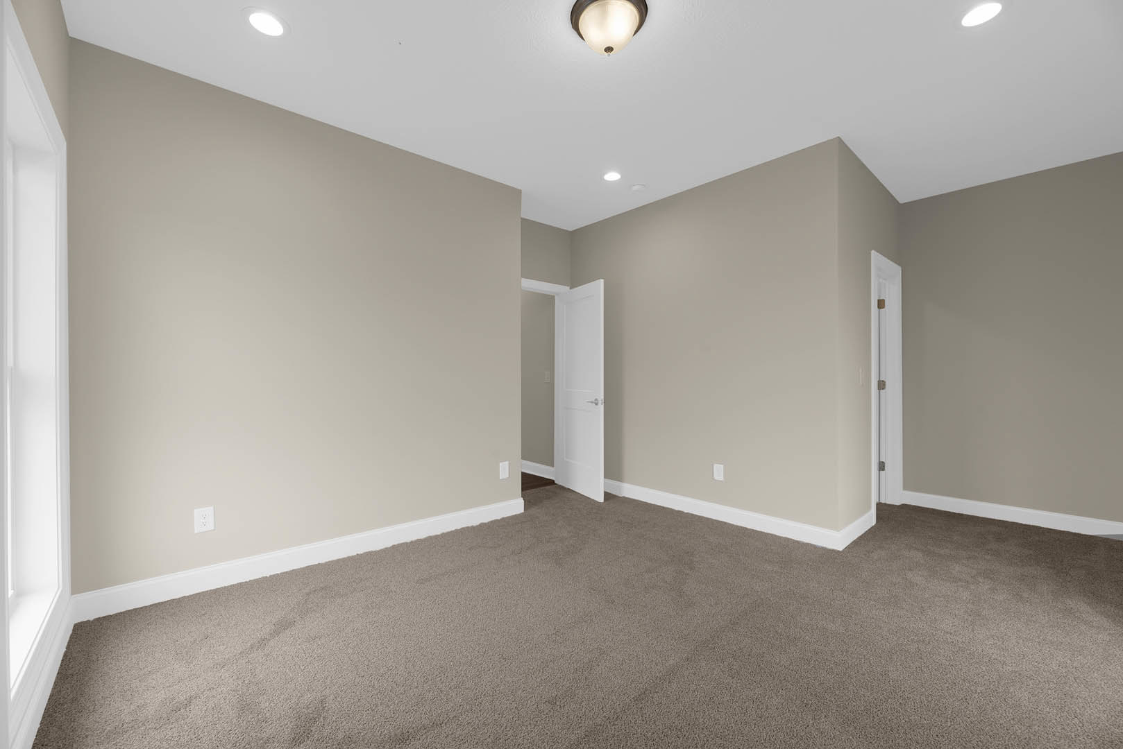 Beige walls, white door with silver handle, plush carpet flooring, ceiling light fixture, white baseboards and molding