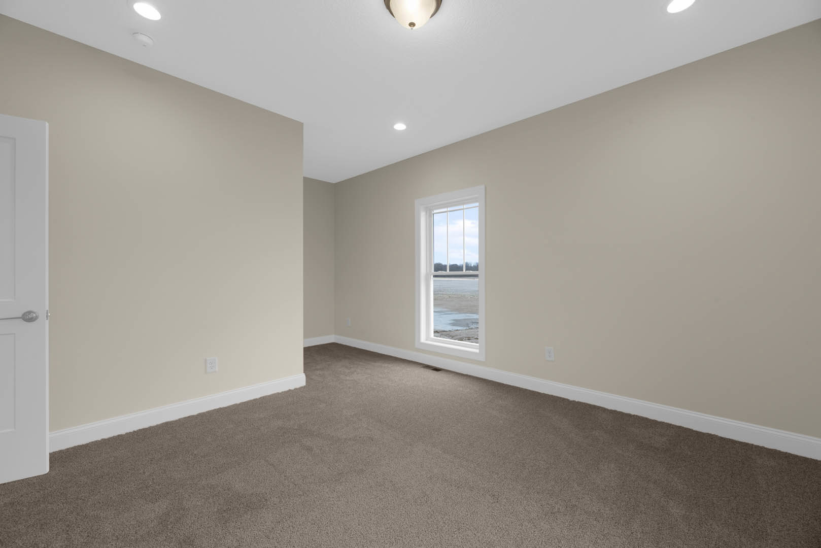 Carpeted bedroom with white walls, large window overlooking the ocean, white paneled door with silver handle, ceiling light fixture, crown molding along ceiling edges