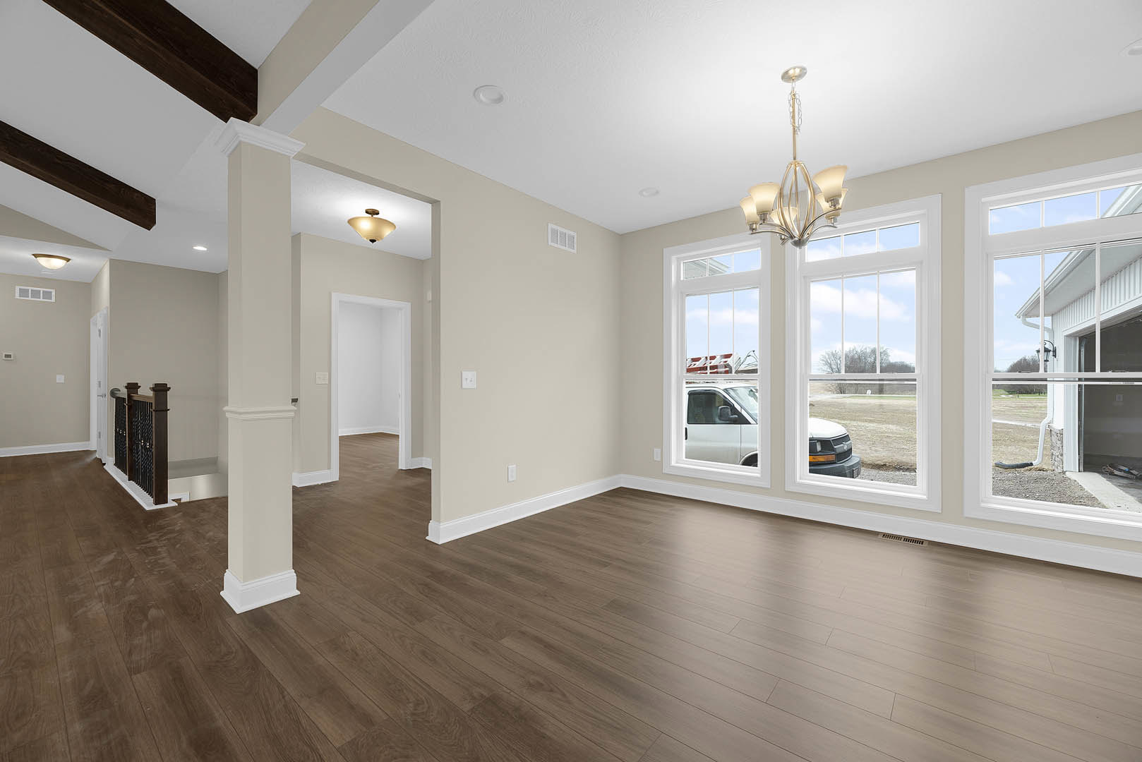 Spacious room with hardwood flooring, white plaster walls, decorative ceiling molding, and a modern chandelier hanging from the ceiling