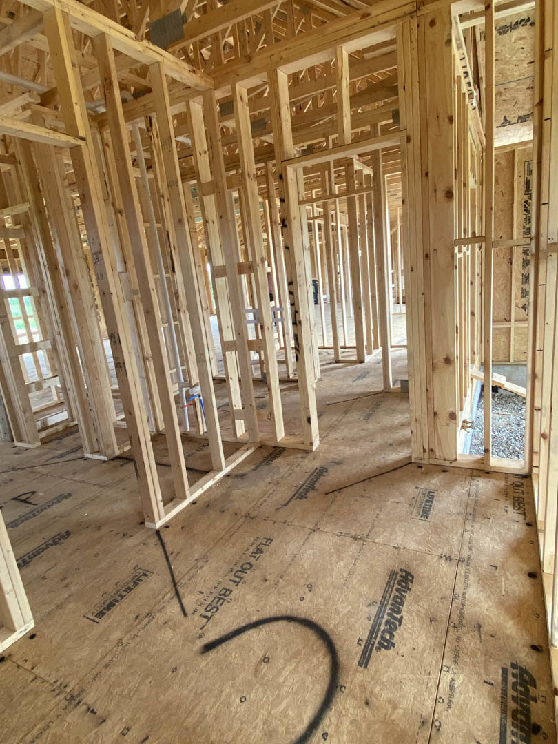 Exposed wood framing and beams with construction materials scattered on unfinished floor, visible insulation between studs, natural light filtering through open ceiling structure