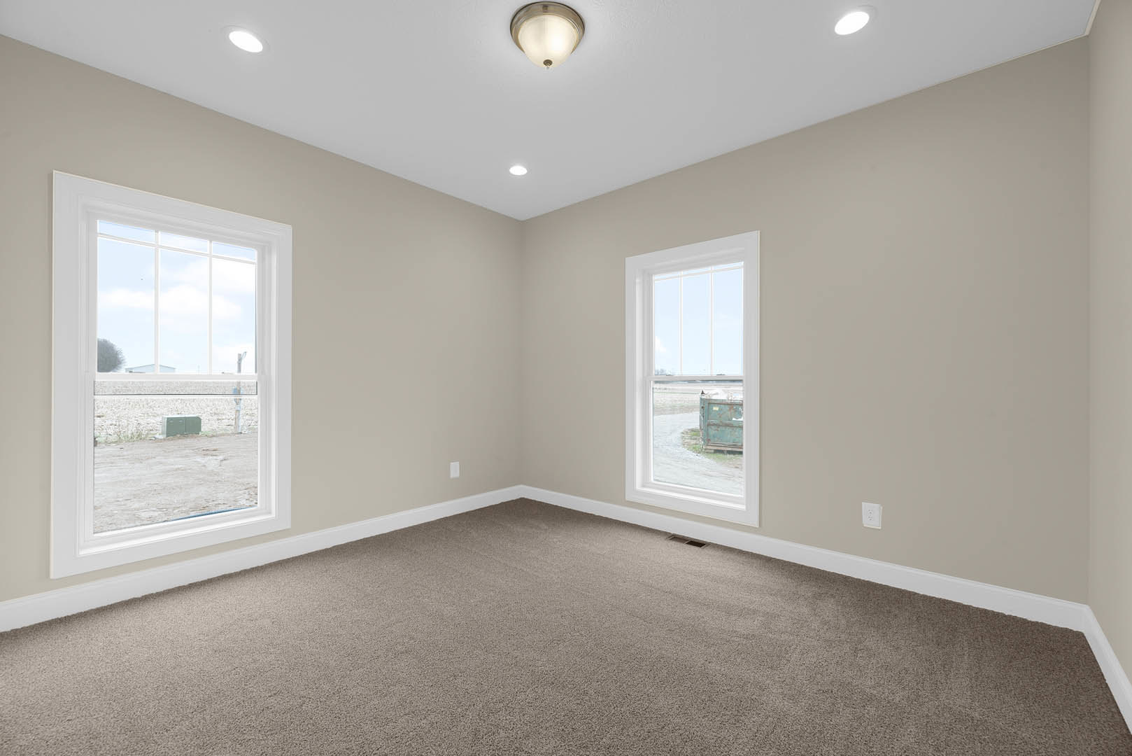 Carpeted room with large windows overlooking a grassy field, white walls with crown molding, ceiling-mounted light fixture, and blue dresser visible outside the window.