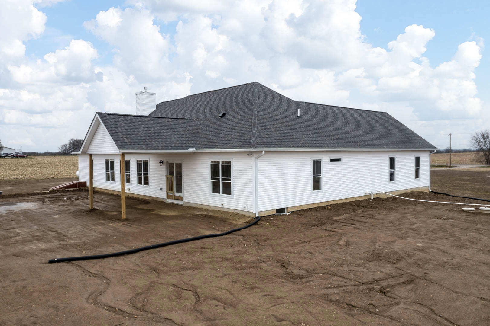 White house under construction with exposed roof, black hose extending from entry, unfinished exterior walls, cloudy sky overhead