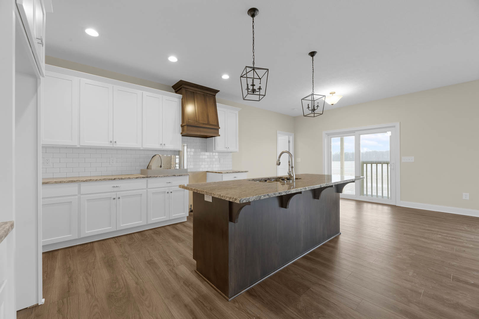 Open kitchen with wood flooring, central island featuring built-in sink, white lower cabinets topped by wooden upper cabinetry, glass door leading to dining area with table