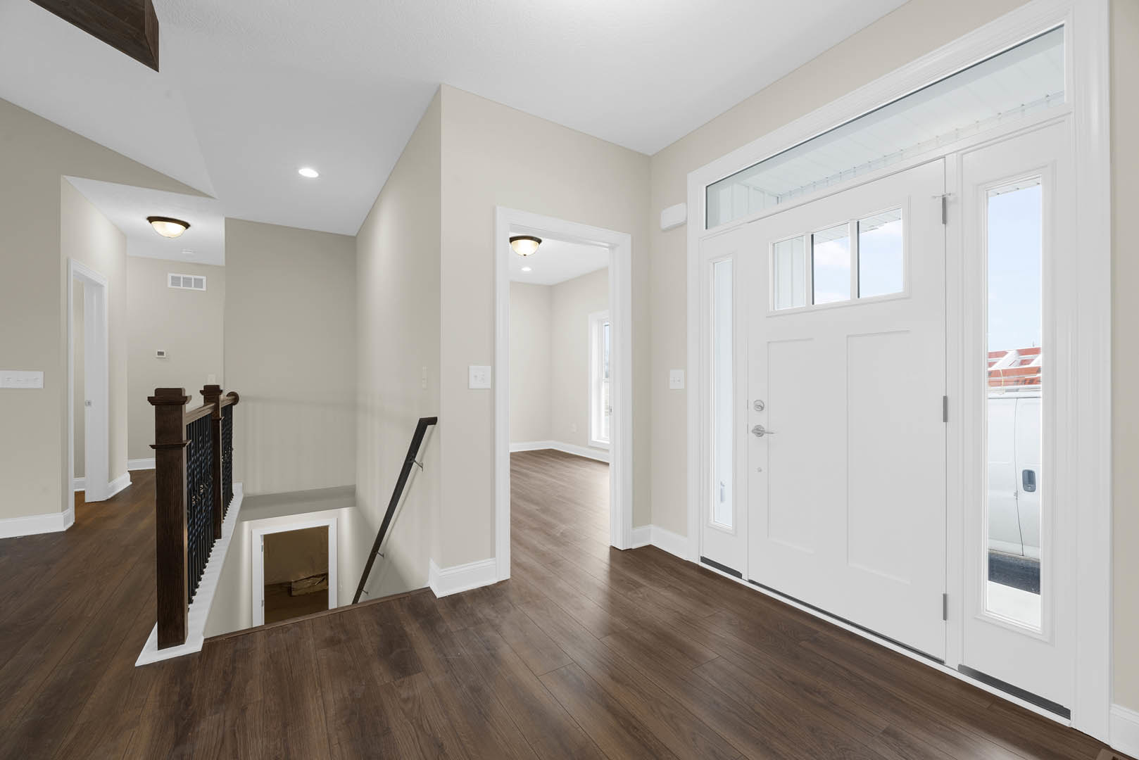 Hallway with wood flooring and white trim, staircase with wooden railing, white door with glass windows, plaster walls, visible pipe and window with paper attached