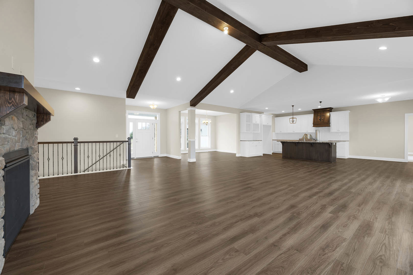 Spacious room featuring wood flooring, white plaster walls, exposed ceiling beams with recessed lighting, modern black railing, and a wooden cabinet suspended by a visible wire.
