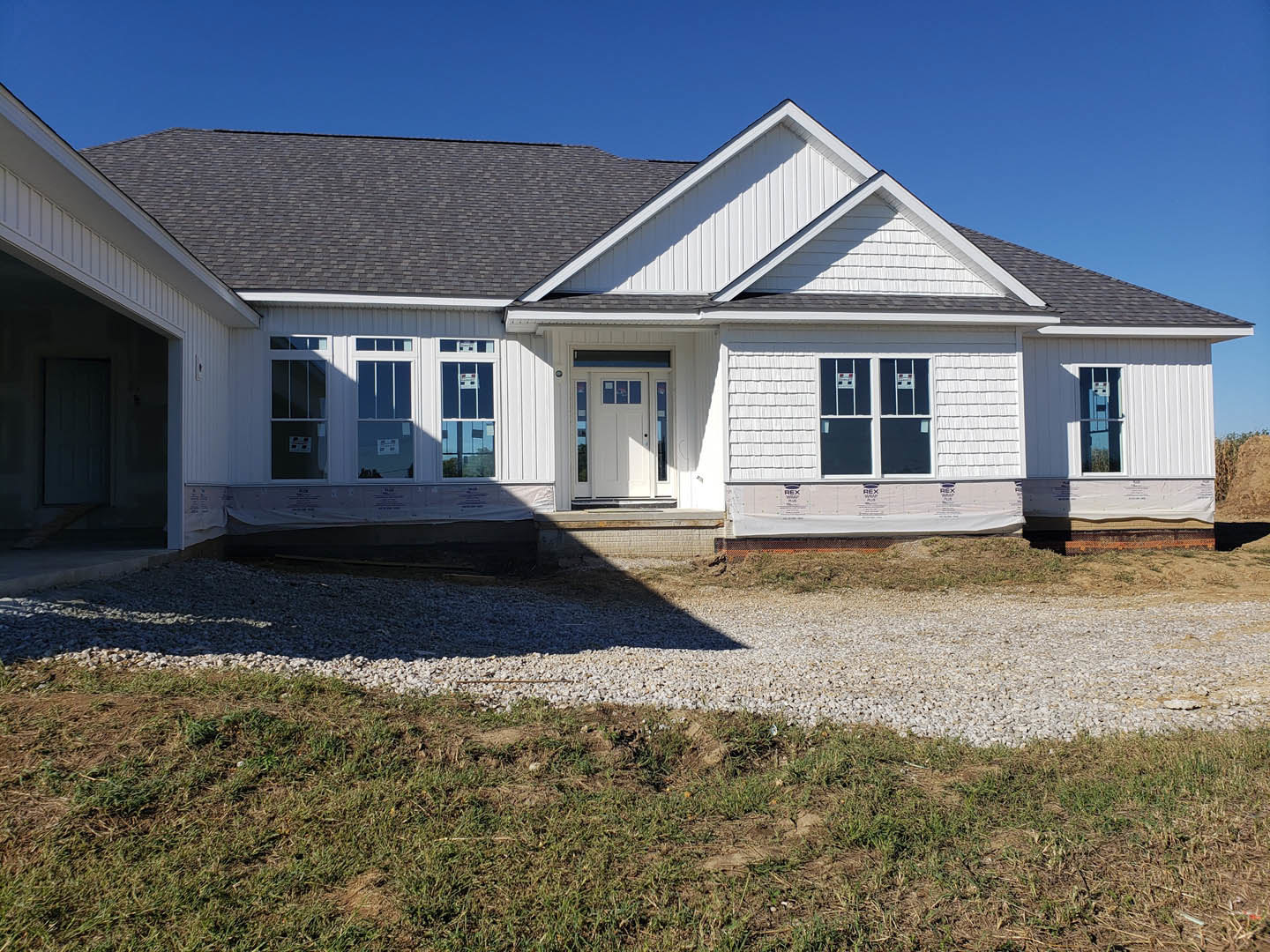 Two-story house with light siding, white framed windows, glass-paneled front door, concrete driveway, and green lawn under clear blue sky