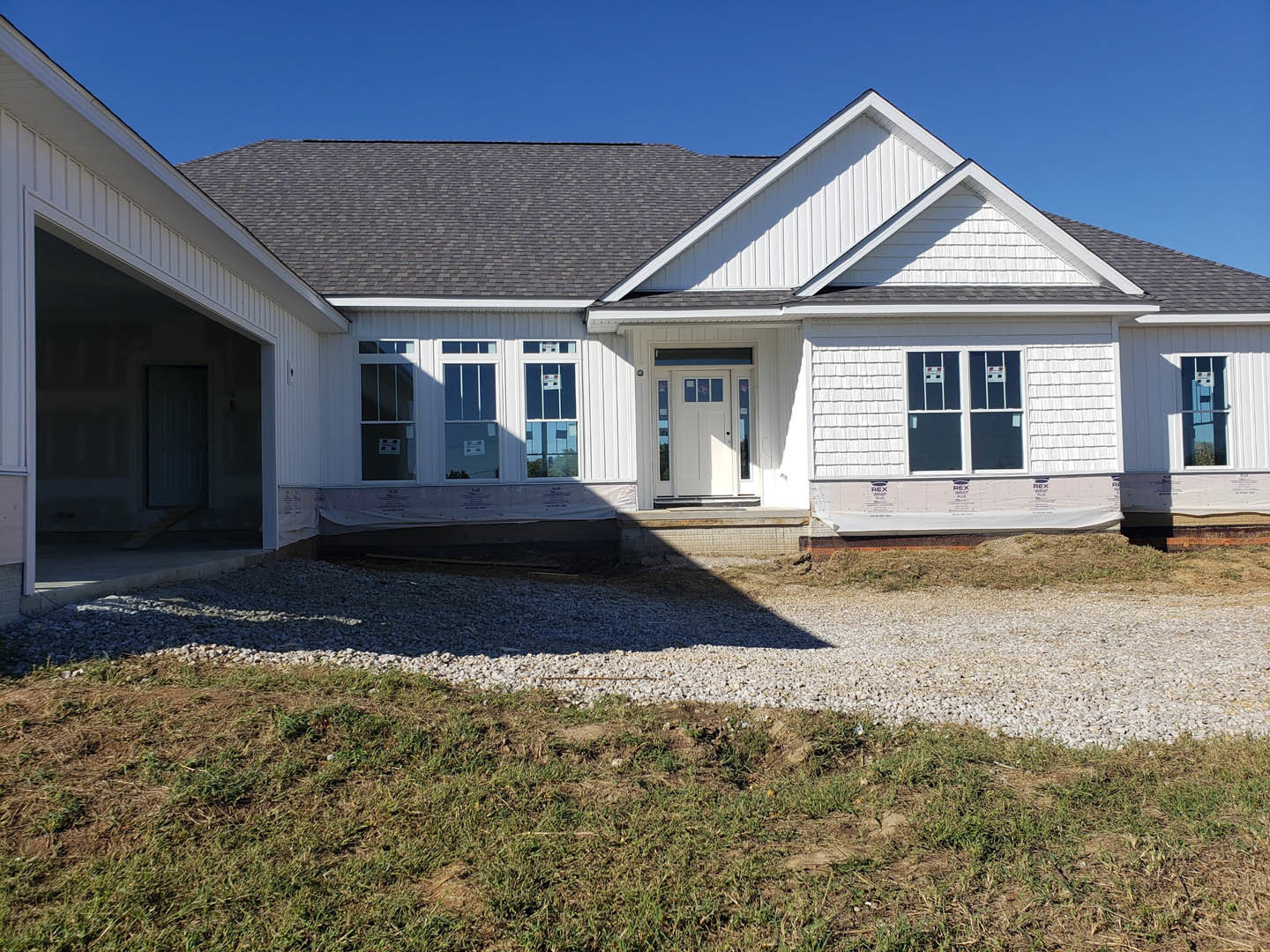 Two-story house with light siding, white door with glass panes, barred window, driveway, small patch of grass, and blue sky overhead