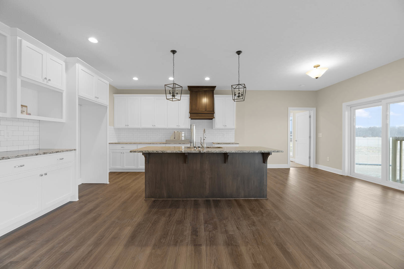 Spacious kitchen featuring a marble-topped island, wooden cabinetry with under-cabinet lighting, wood flooring, open shelving, and a white door framing an ocean view.