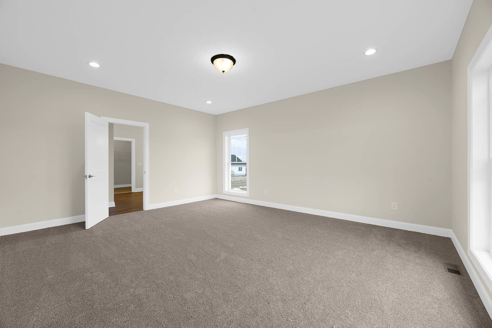 Carpeted bedroom with open white door, ceiling-mounted light fixture, window overlooking neighboring house, white walls with crown molding