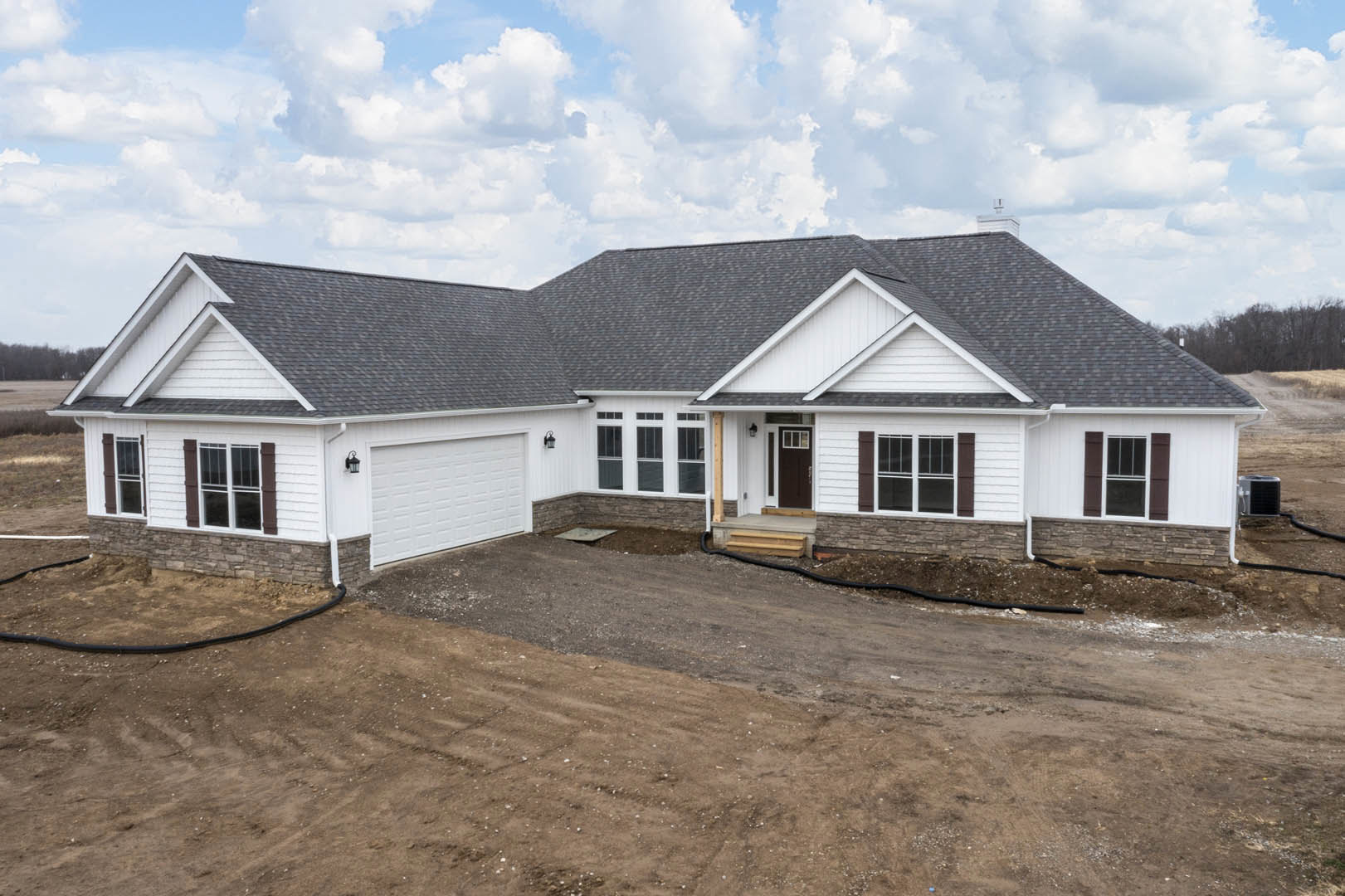 Two-story home with light siding, attached garage, white-framed windows, and a dirt driveway under a cloudy sky