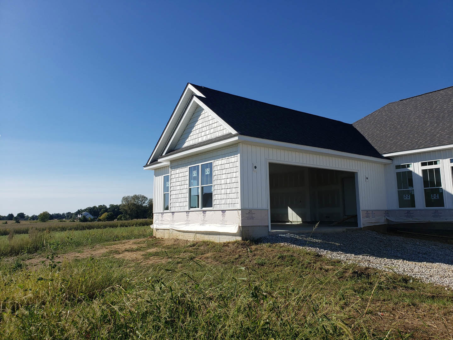 White modern house under construction with black roof, attached garage, large windows, and grassy yard.