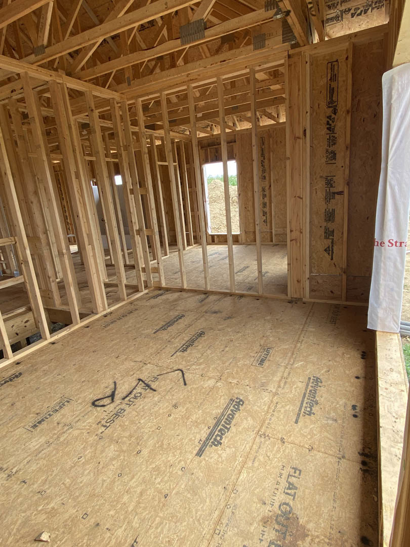 Unfinished room with exposed wood framing, two windows, construction materials on floor, and visible ceiling beams