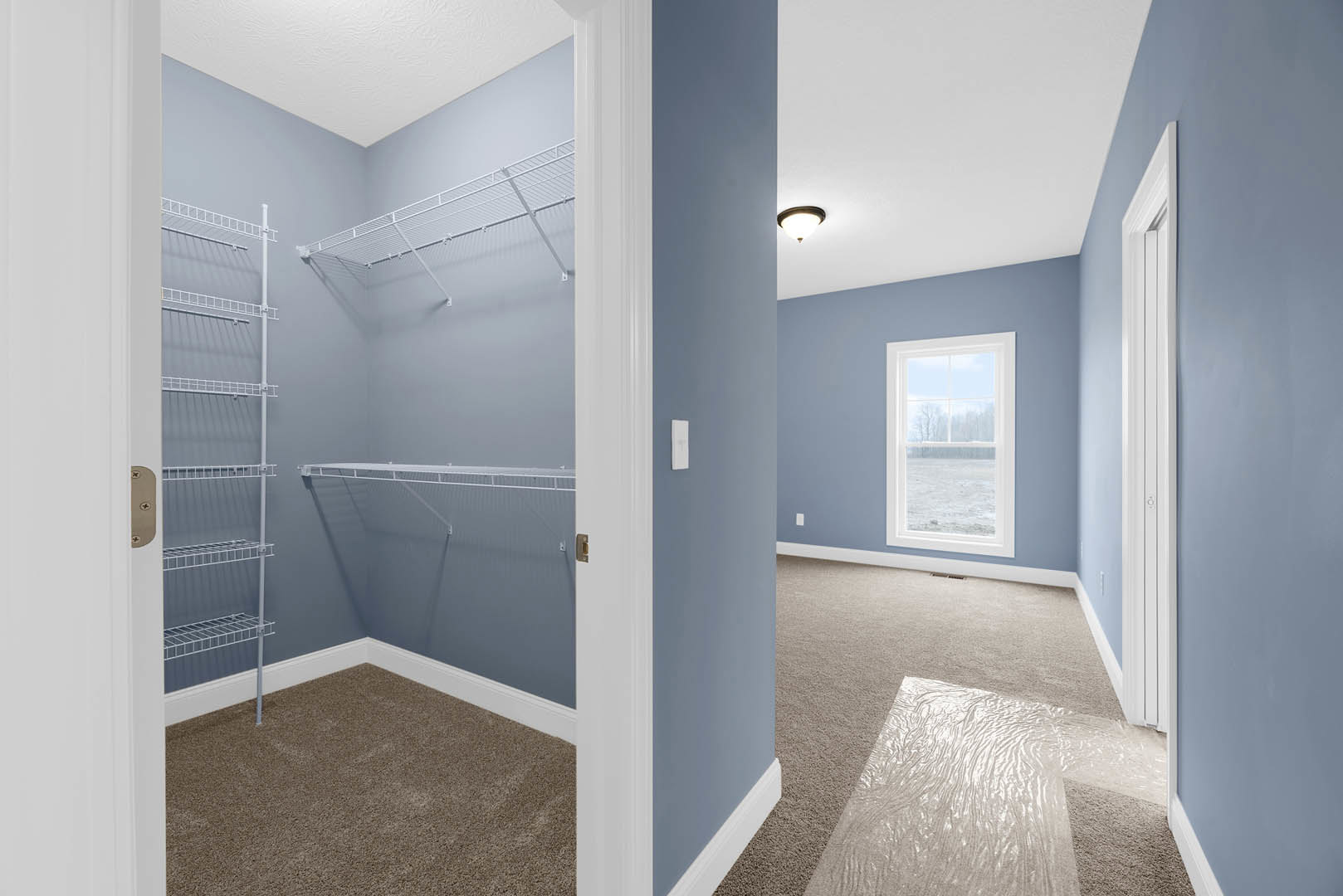Walk-in closet with white shelving, tile flooring, plaster walls, ceiling light fixture, window overlooking snowy field, white metal fence visible outside