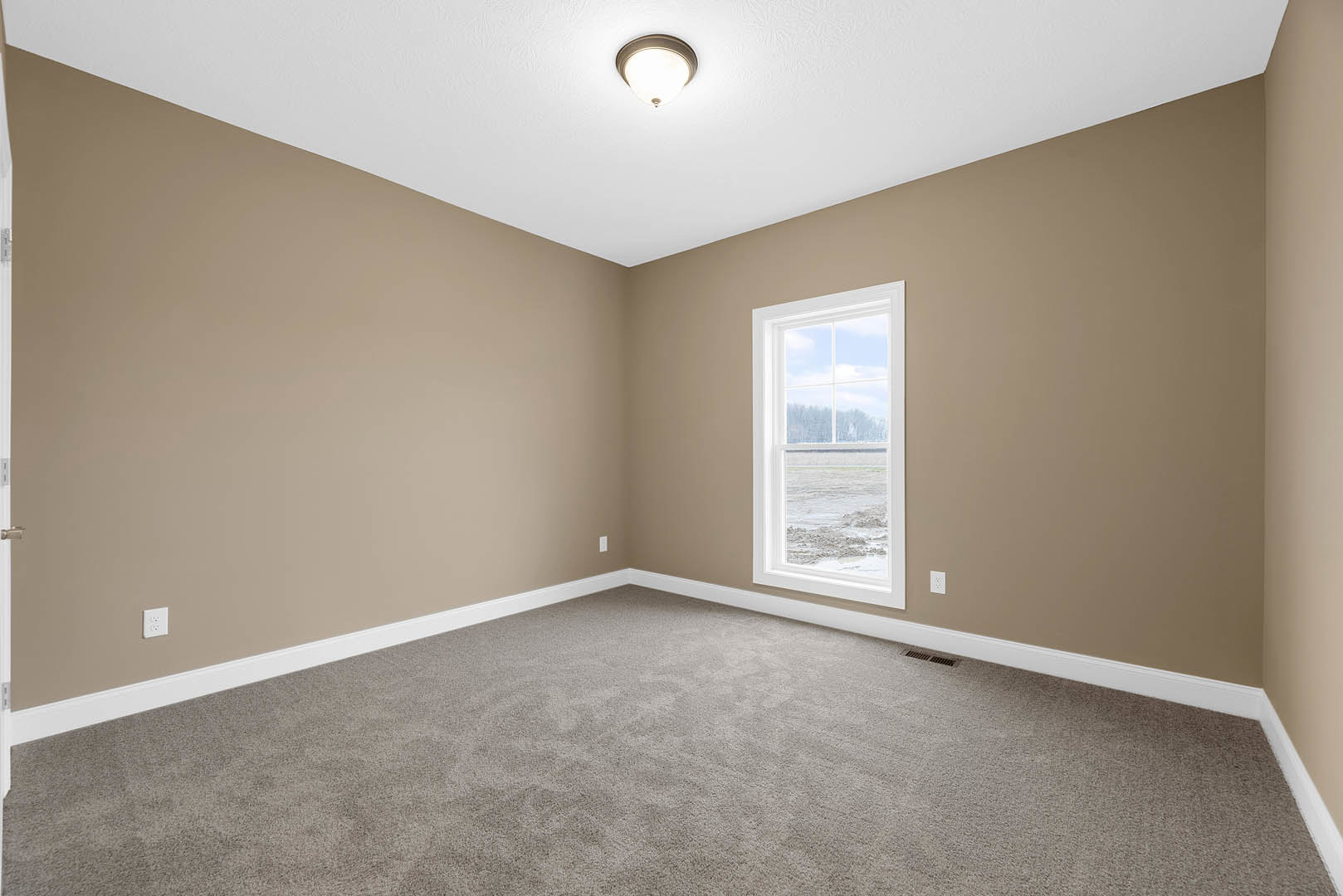 Carpeted room with white walls, large window overlooking snowy forest, ceiling light fixture, and decorative molding