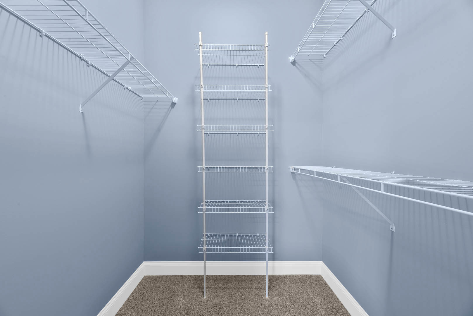 Carpeted room with multiple white wire shelves mounted on white plaster walls, white baseboards, and a white metal handrail