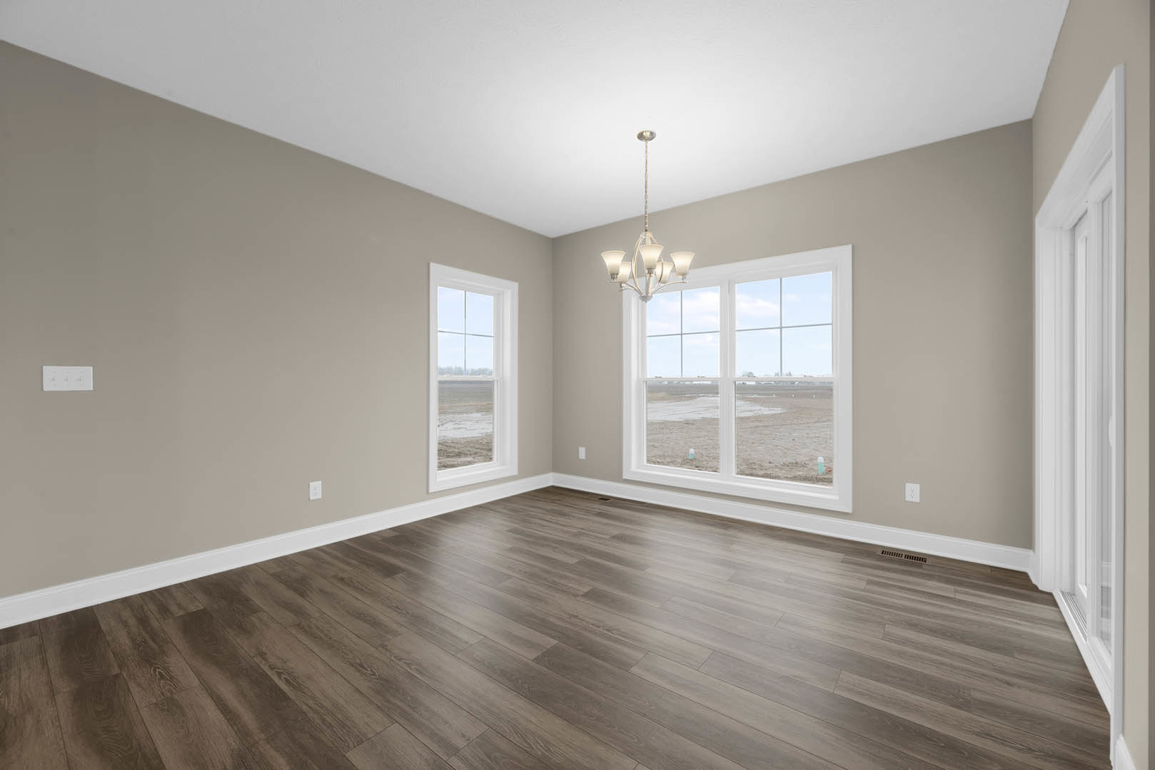 Spacious room with wood flooring, large windows, white walls, and a modern chandelier; windows offer views of beach and field.