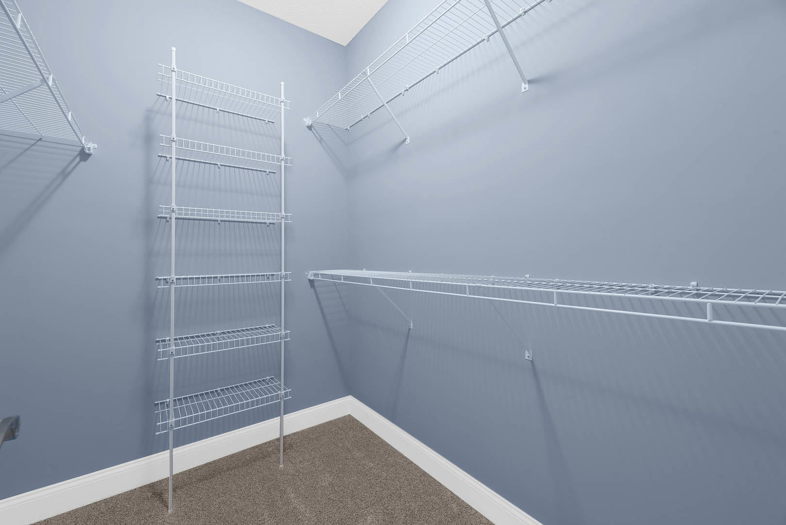 White plaster bathroom wall with built-in white metal shelves, close-up of shelving pole and shelf surfaces.