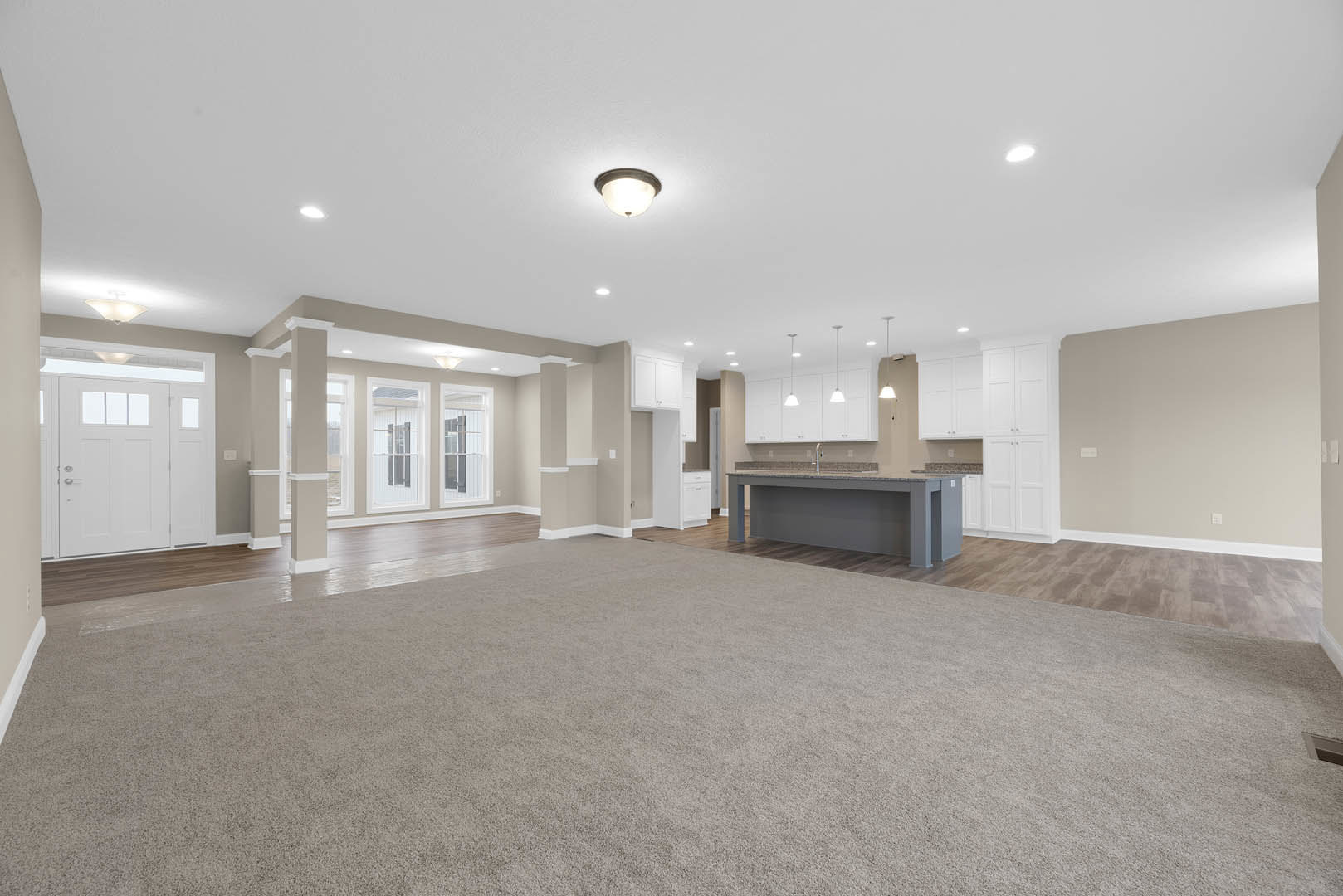 Open concept kitchen and dining area with carpeted floor, stone countertop and sink, pendant light fixtures, white door with glass panes, plaster walls, and fireplace.