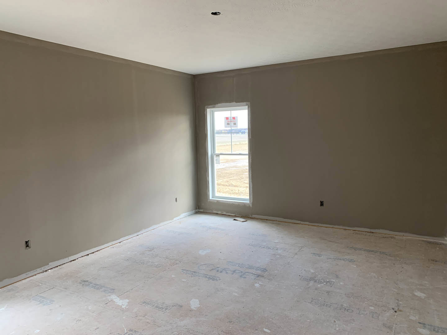 Bright room with white plaster walls, white ceiling, and white floor; large window with white frame offers outdoor view; black ceiling fixture suspended near window