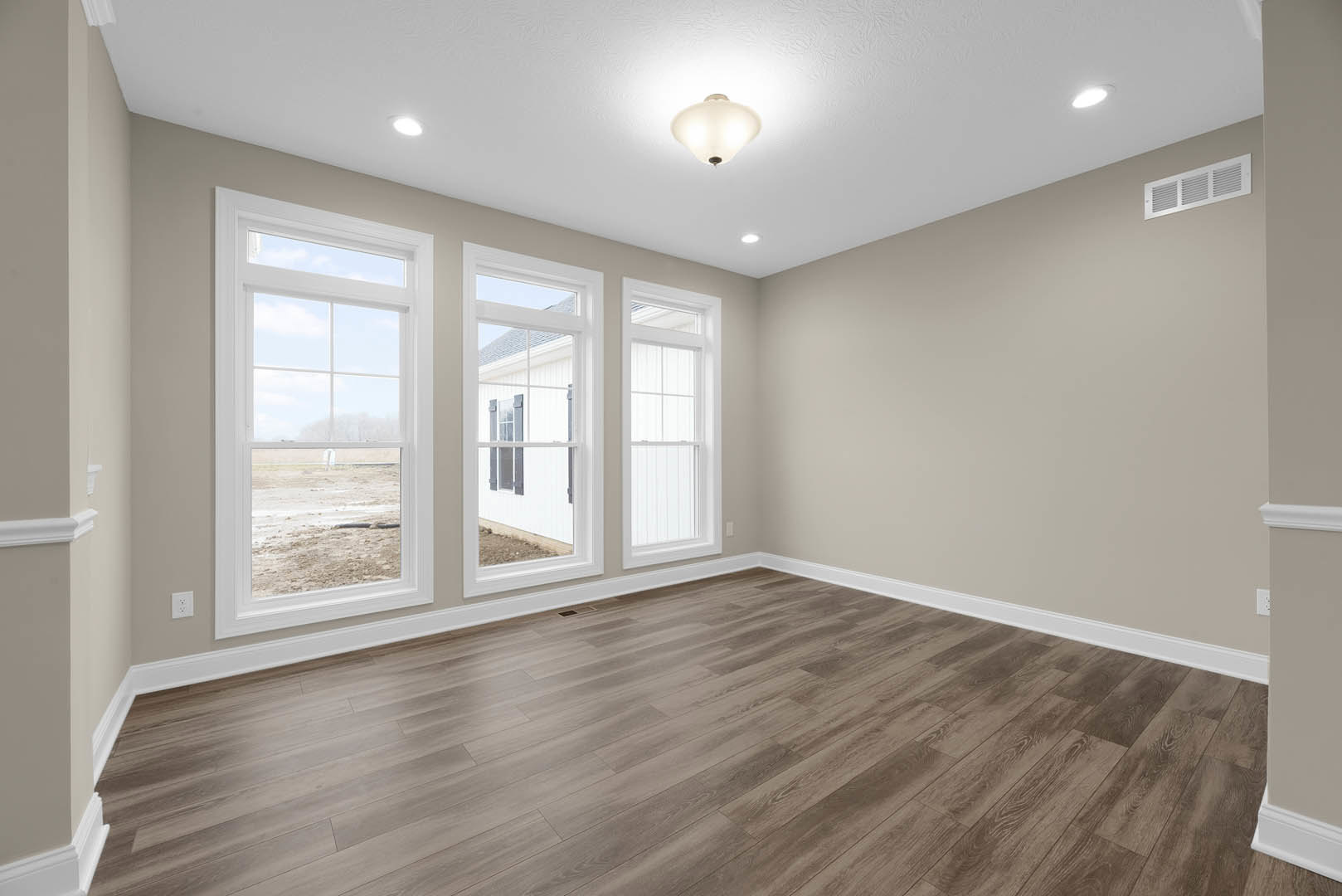 Spacious room with wide plank wood flooring, large windows framed by white walls, ceiling light fixture, and outdoor view through glass panes