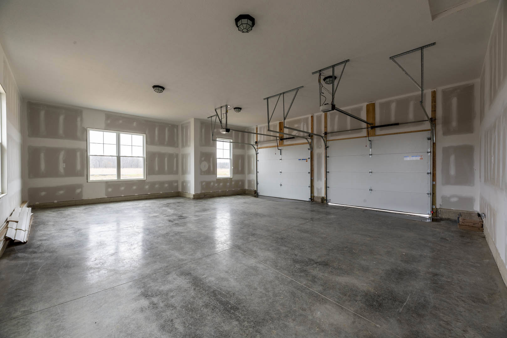 Spacious room with smooth white plaster walls, concrete floor, multiple windows, white door, and ceiling light fixture
