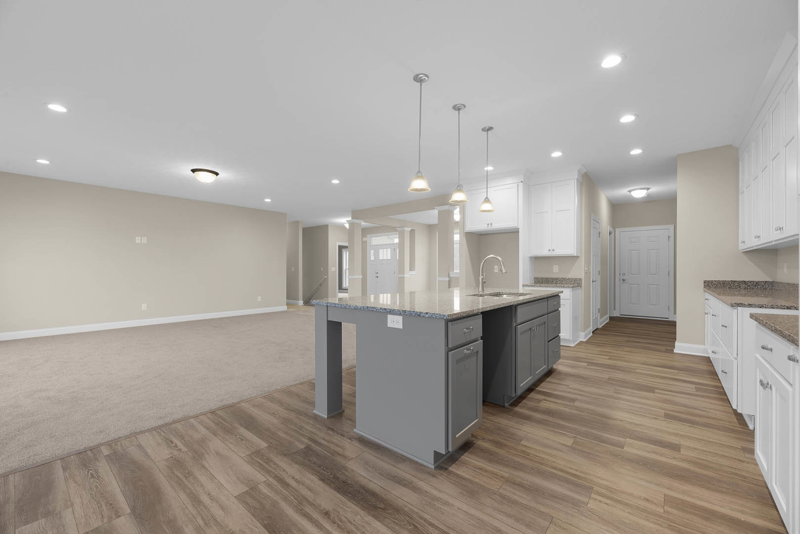 Open kitchen and living room with hardwood flooring, white cabinetry, marble kitchen island countertop, stainless steel sink, silver door handles, ceiling pendant lights, and white