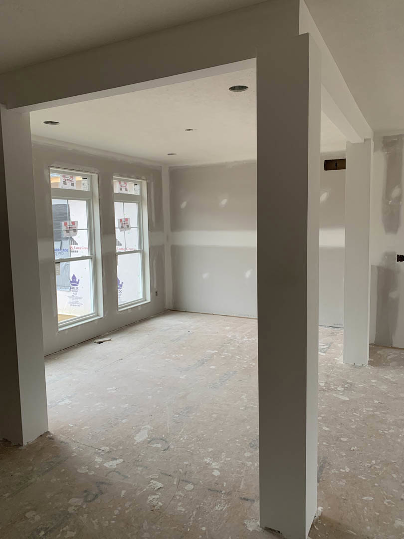 Spacious room featuring white columns, large windows with white trim, light-colored walls, and hardwood flooring