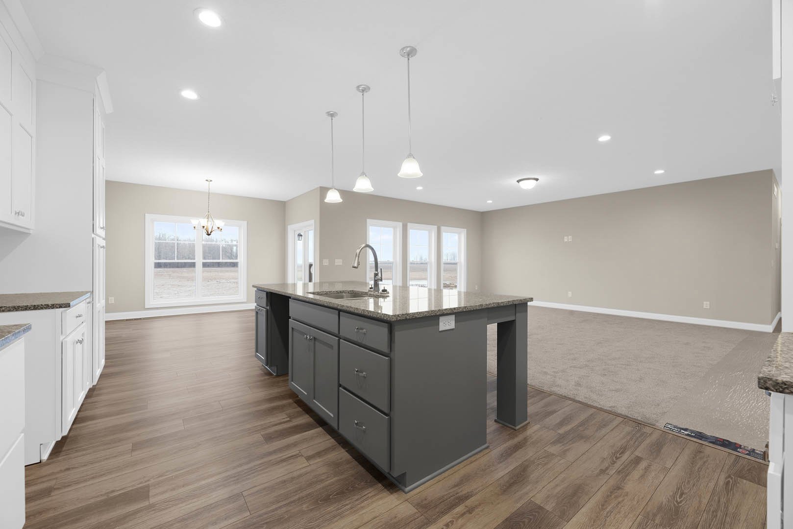 Marble kitchen island with built-in sink and chrome faucet, white cabinetry, wood flooring, large window, and modern chandelier overhead.
