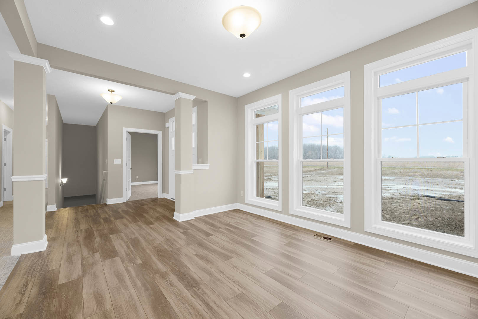Wood floor with white trim, white walls, large windows overlooking a field, white door, and grey accent wall