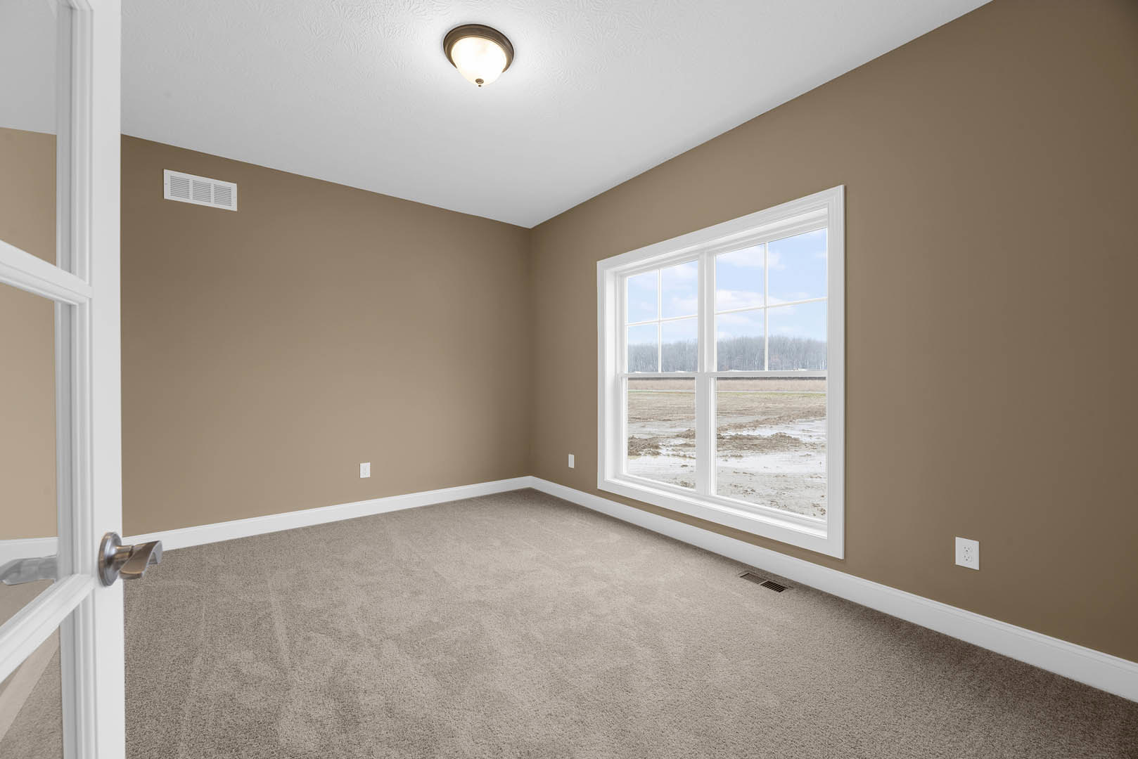 Carpeted bedroom with white walls, large window overlooking grassy field, ceiling light fixture, wall vent, and white door frame molding