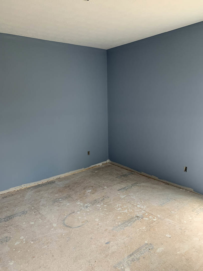 Blue accent wall, polished concrete floor with faint tire marks, white ceiling, black trim in room corner