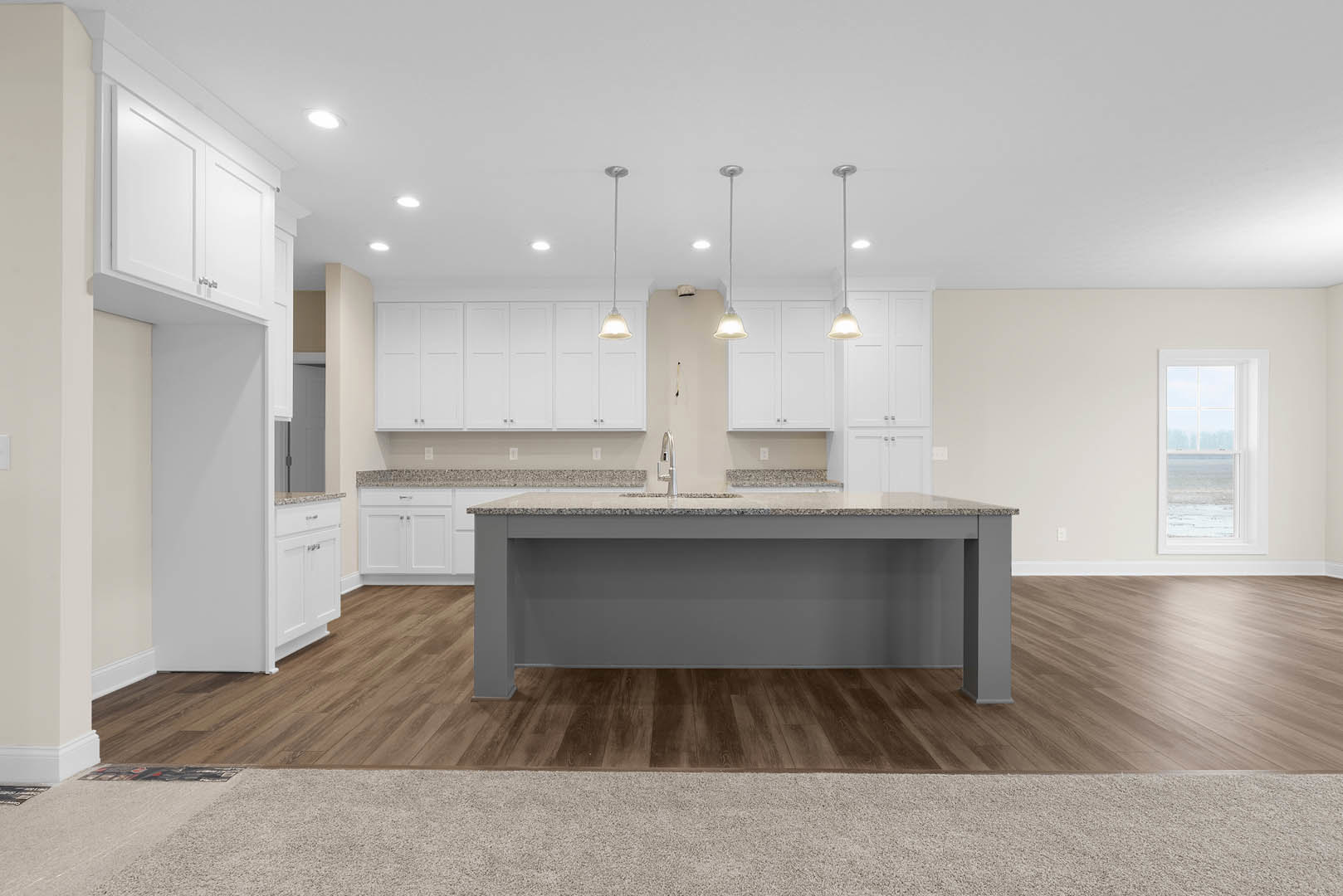 Spacious kitchen featuring a large granite island with built-in sink, white cabinetry, wood flooring, and a window overlooking the ocean; carpeted area visible in foreground.