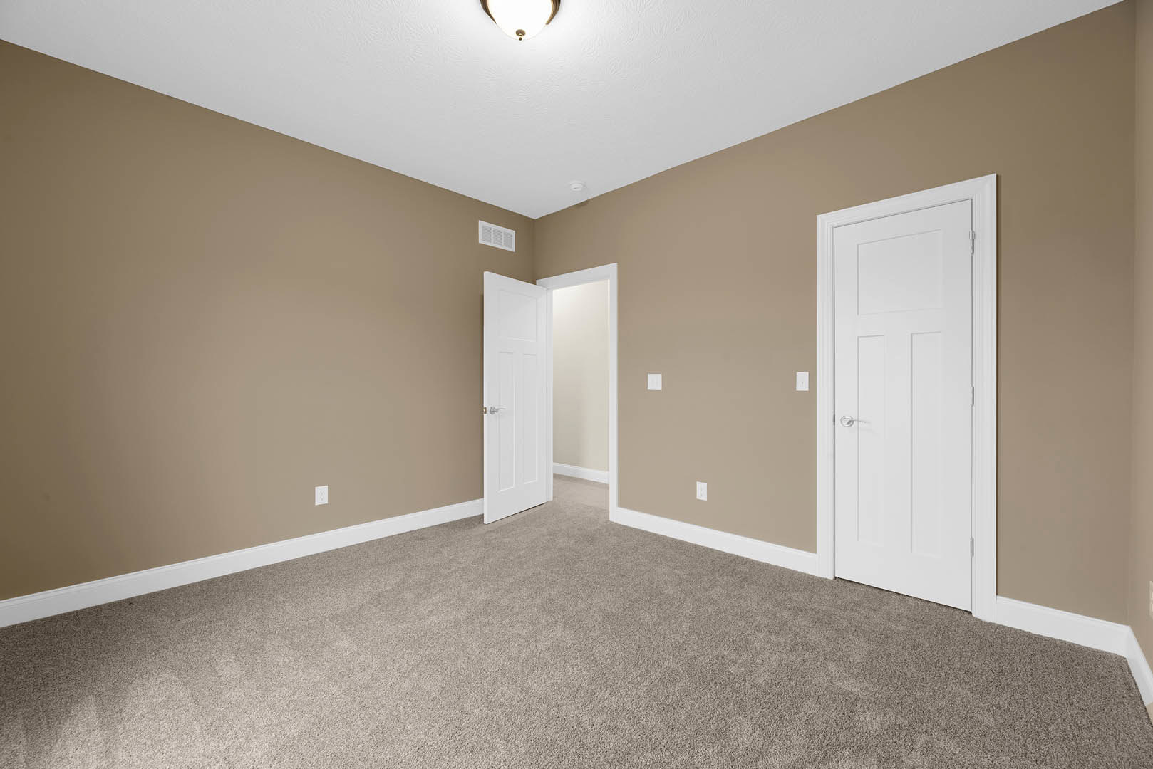 Beige-walled room with two white doors featuring silver handles, plush light carpet flooring, white ceiling with recessed lighting, and simple molding trim