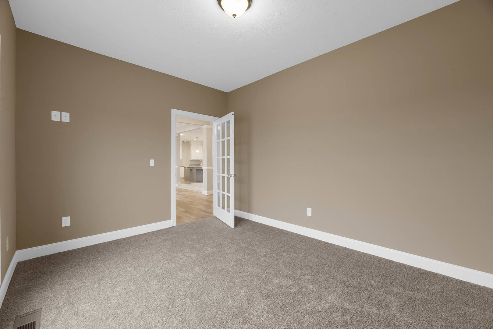 Open white door leading to kitchen and dining area with laminate flooring, plaster walls, ceiling light fixture, and crown molding.