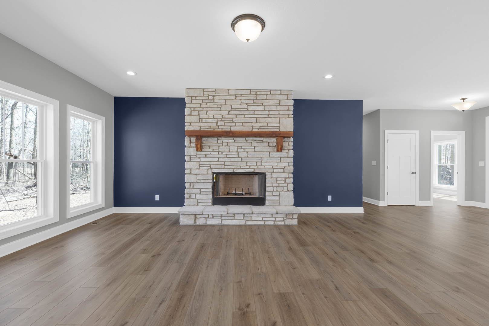 Living room with black-framed fireplace, wood mantel, hardwood floors, white door with silver handle, and ceiling light fixture