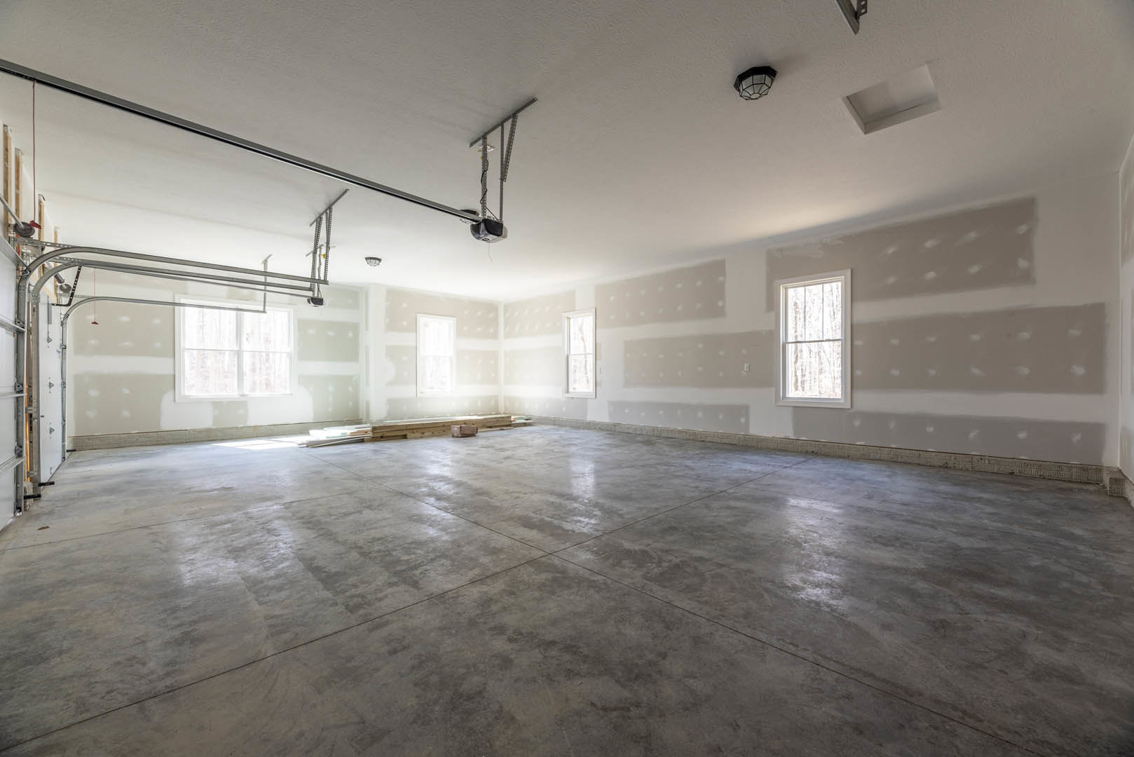 Concrete floor with white plaster walls, large windows with sheer white curtains, black and white ceiling light fixture, minimalist and empty interior space
