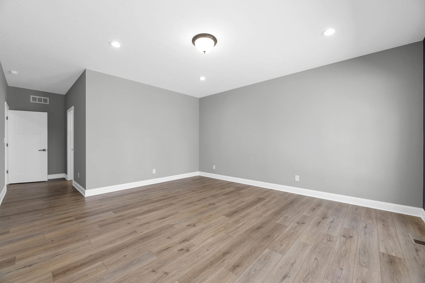 Wood flooring in a room with white walls, black door handle, and modern ceiling light fixture