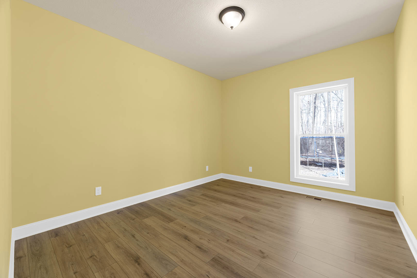 Room with hardwood floor, white-framed window, ceiling light fixture, and indoor trampoline with safety net.