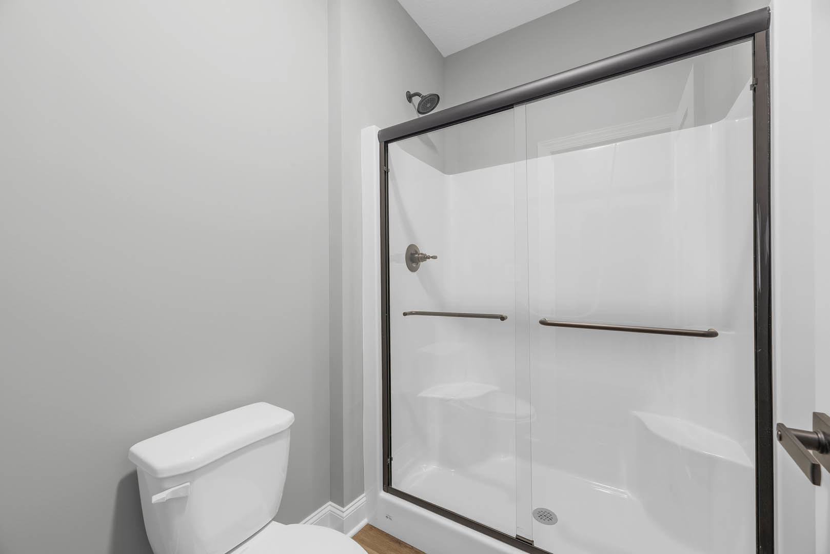 Modern bathroom featuring a frameless glass shower enclosure, white tile walls, chrome faucet and shower head, sleek toilet, and large wall mirror.