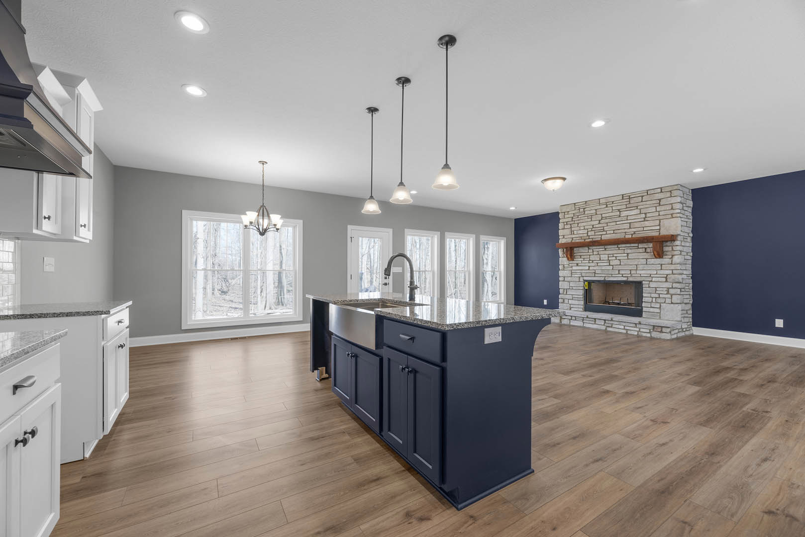 Kitchen featuring a stone fireplace with wood mantel, stone accent wall, granite island countertop, marble perimeter counters, cabinetry, and window with pendant light fixture