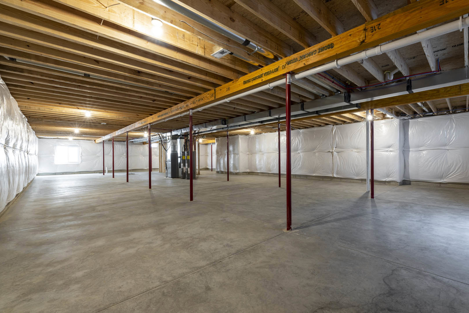 Wooden ceiling with exposed beam, metal pole framed with wood, concrete floor featuring red support poles, stack of white plastic bags near a bed draped with a white blanket in an