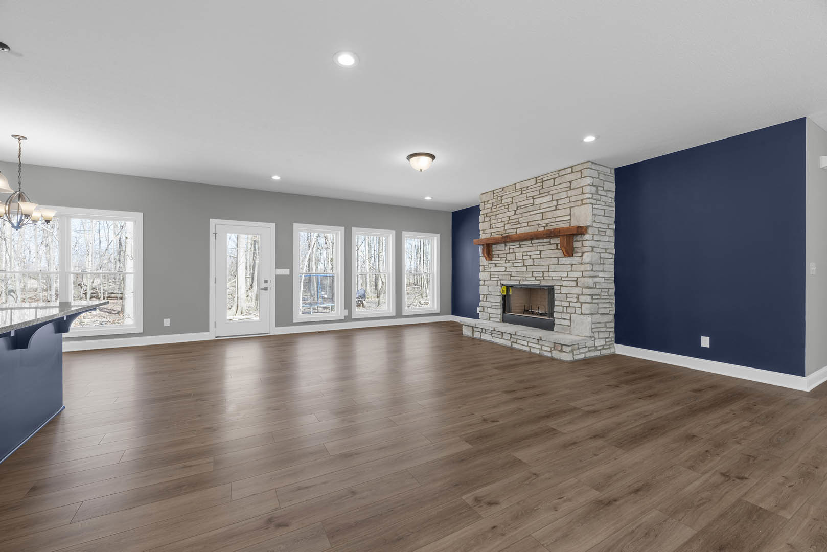 Fireplace with white mantel, blue accent wall, hardwood floors, ceiling light fixture, white door with glass window, plaster ceiling