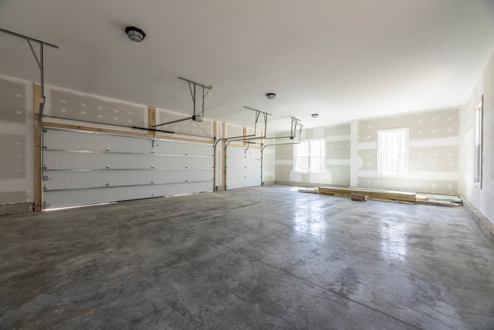 Concrete floor with white plaster walls, white-framed window, white garage door with metal rails, wall-mounted light fixture, basketball hoop above window.