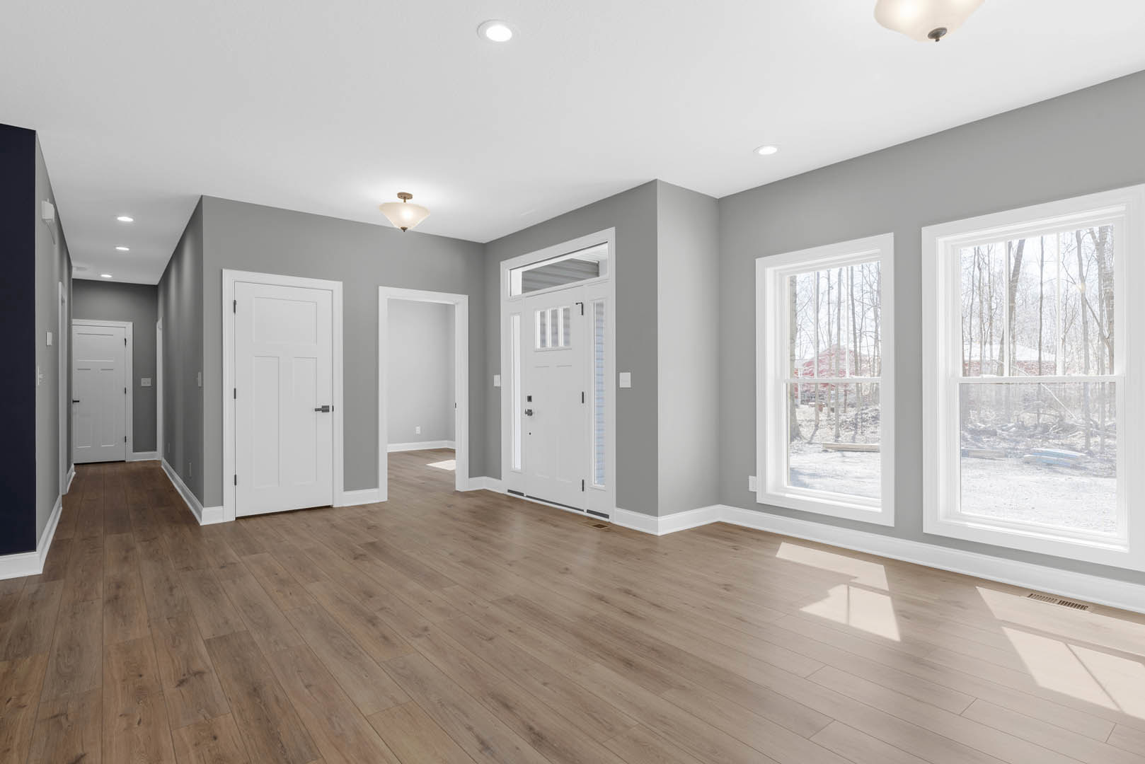 Hardwood floor room featuring a white door with glass panels and black handle, large window overlooking forest, white walls and ceiling