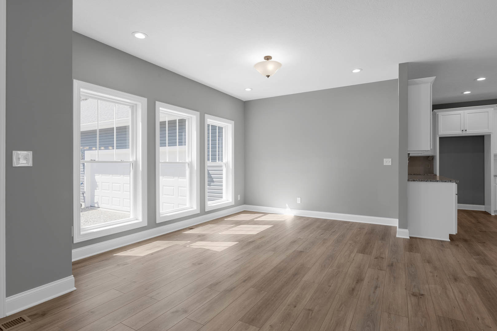 Spacious room with hardwood flooring, large windows along one wall, white plaster walls, and a floor vent near the windows