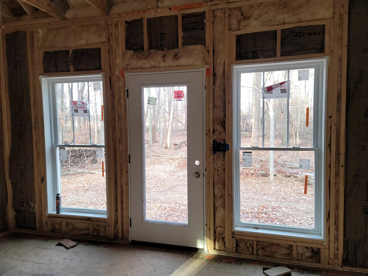 Bright room with light wood flooring, two large windows with white trim, and a glass-paneled door, all set against neutral painted walls