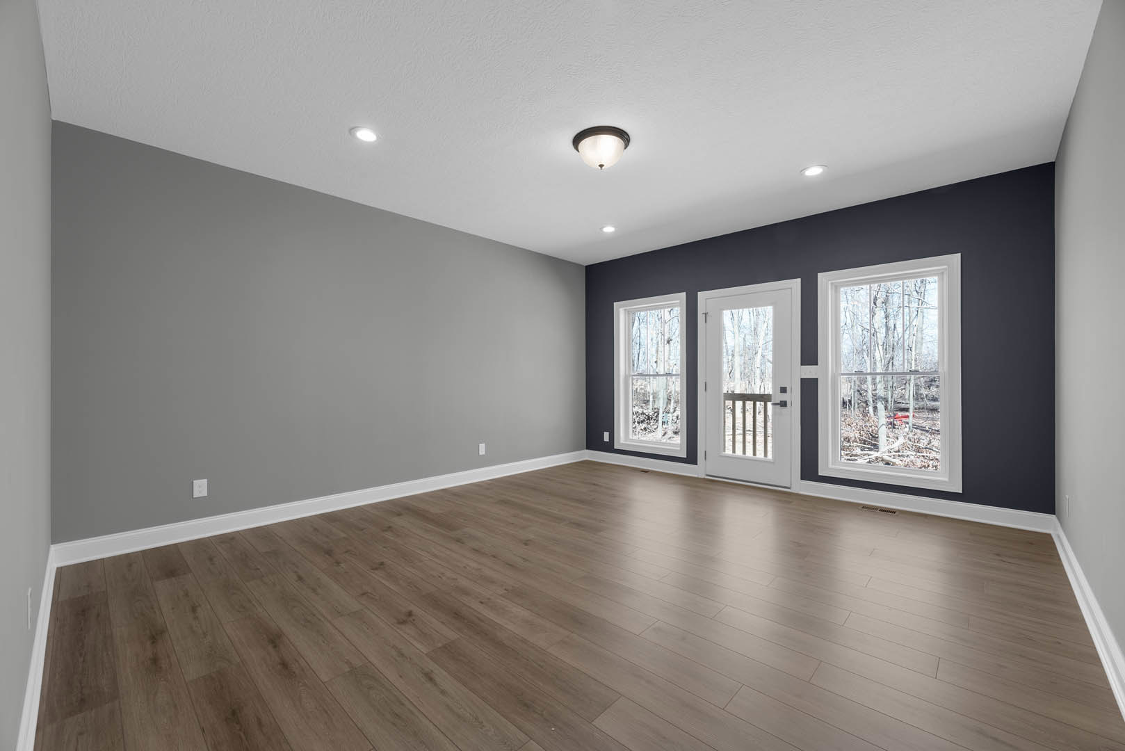 Hardwood floor room with white-framed windows showing trees outside, glass-paneled door with railing, plaster walls, ceiling light fixture