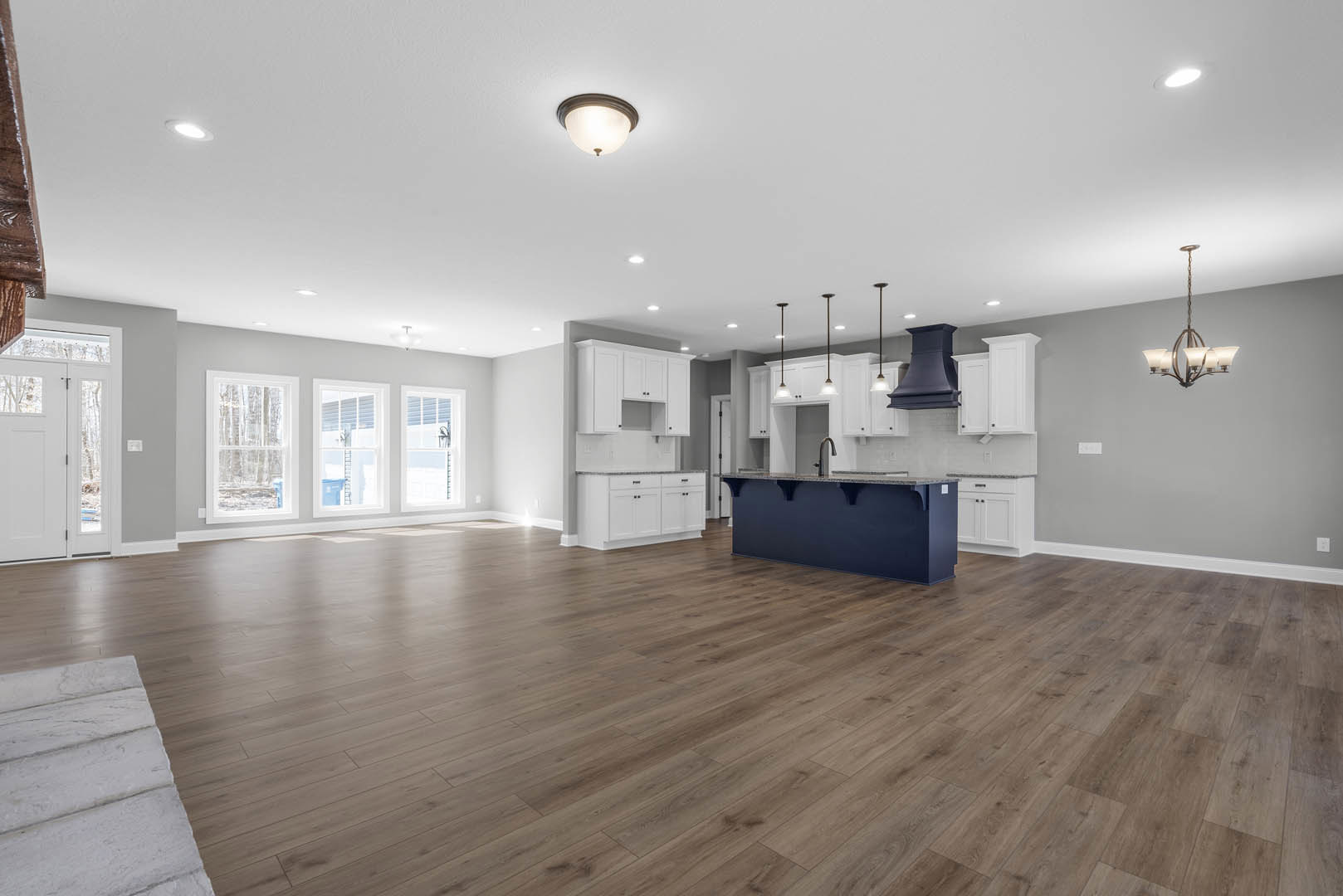 Open kitchen with blue island, white cabinetry, hardwood floors, and chandelier with white shades